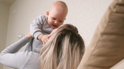 Kid and mother play together, fantasize and dream of flying on plane. Young mom raising cute little baby, daughter playing pilot on sofa at home. Funny little son flying in mother s arms. Happy family