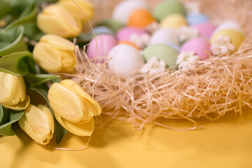 multicolored easter eggs on hay and near yellow tulips on yellow background