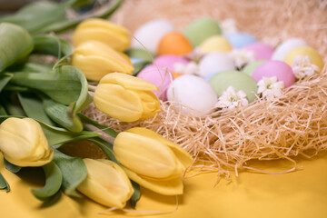 Fototapeta na wymiar multicolored easter eggs on hay and near yellow tulips on yellow background