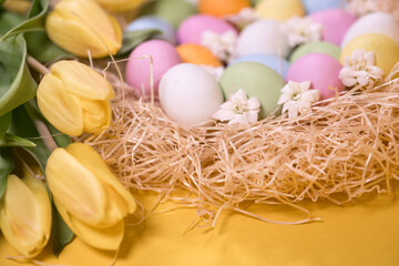 multicolored easter eggs on hay and near yellow tulips on yellow background
