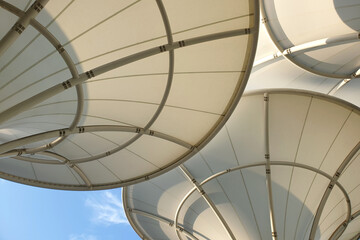Low angle view huge canopies tensile membrane structure against the sunny blue sky. - obrazy, fototapety, plakaty