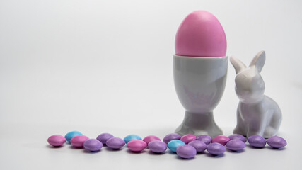 Side view of  Porcelain Egg Cup with pink Easter egg and  porcelain Easter bunny and same pastel colored chocolate candy.On a white background .