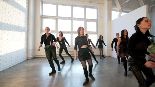 Young women in black costumes are performing modern shuffle dance in the studio