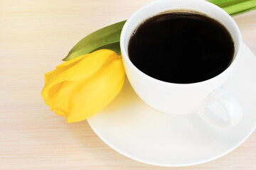 A yellow tulip sits on a white saucer next to a cup of coffee. Wallpaper