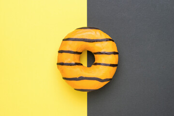Orange glazed donut on the border of yellow and black colors.