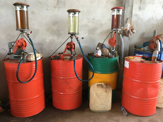 Fuel dispenser machines and large metal barrels with gasoline at a filling station.
