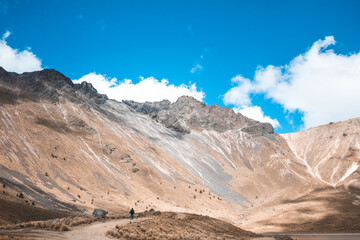 Adult man in the distance admiring the rocky landscape of the mountains partially covered with snow in the middle of a sunny day and with blue sky