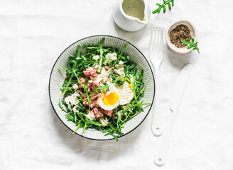 Salad with arugula, canned tuna, boiled egg and yogurt, mustard dressing on a light background, top...