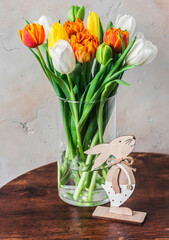 Easter still life. Bouquet of colorful tulips in a glass vase and a wooden Easter bunny decoration on the table