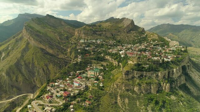 Aerial backwards epic historical traditional village Gunib aul Dagestan amazing Russia. Settlement on top high mountain, winding alpine serpentine road. Cumulus awe-inspiring clouds, summer. Original