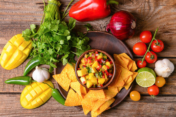 Composition with fresh mango salsa and nachos on wooden background