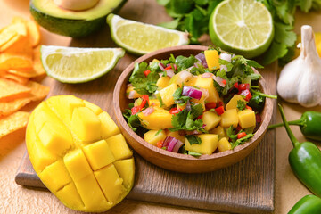 Bowl with fresh mango salsa and nachos on color background, closeup