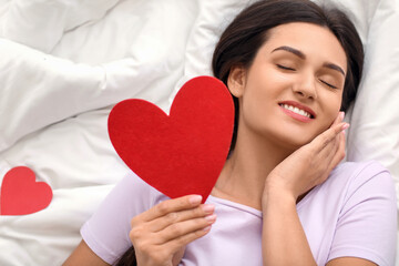 Beautiful young woman with red heart in bed