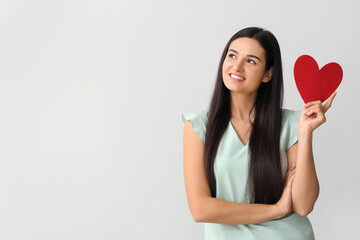 Beautiful young woman with red heart on light background