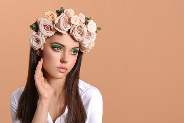 Portrait of beautiful young woman with creative makeup and flowers on head against color background