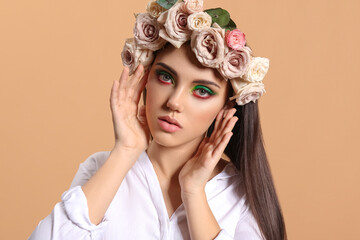 Naklejka premium Portrait of beautiful young woman with creative makeup and flowers on head against color background