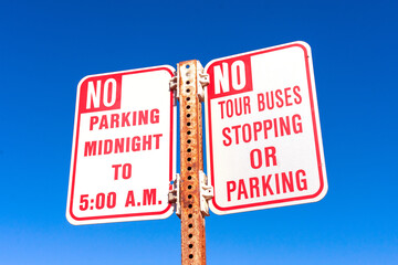 No Tour Buses stopping or parking road sign and No Overnight Parking sign against blue sky.