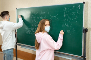Group of students with face mask writing on the board in the classroom during pandemic