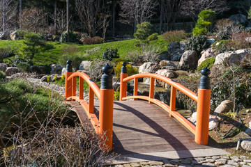 Fragment of a Japanese-style garden with an orange wooden bridge over a mountain stream