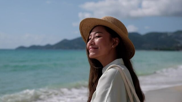 Slow motion of a beautiful young asian woman with hat standing and looking at the sea