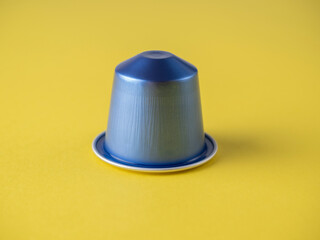 One blue coffee capsule with aromatic Italian coffee on a yellow background. Close-up, front view, capsules for coffee machines.