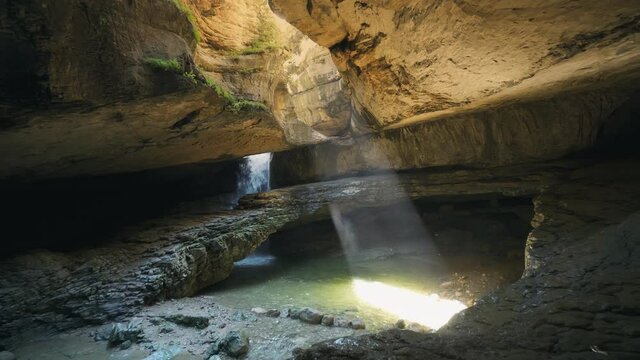 Professional gimbal film fabulous mystical cave cavern underground multi-tiered waterfall, beam of light shines through circular hole in ceiling. Ancient gorge. Speleology, diggers. Untouched nature