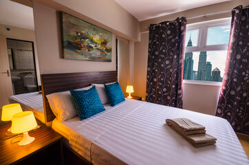 Obraz premium Kuala Lumpur, Malaysia - Feb 2020: Interior of the bedroom of a condominium or hotel with views of Petronas towers and the city skyline.
