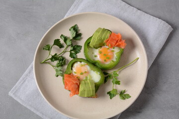 Fried eggs in green bell peppers with avocado and salmon on white plate
