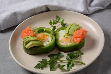 Fried eggs in green bell peppers with avocado and salmon on white plate