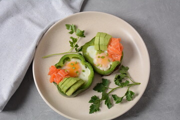 Fried eggs in green bell peppers with avocado and salmon on white plate