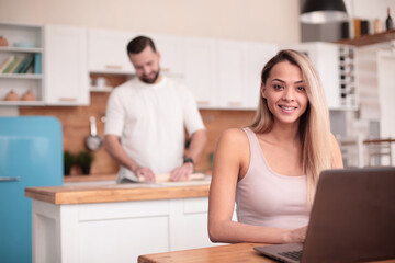smiling female freelancer uses laptop in kitchen