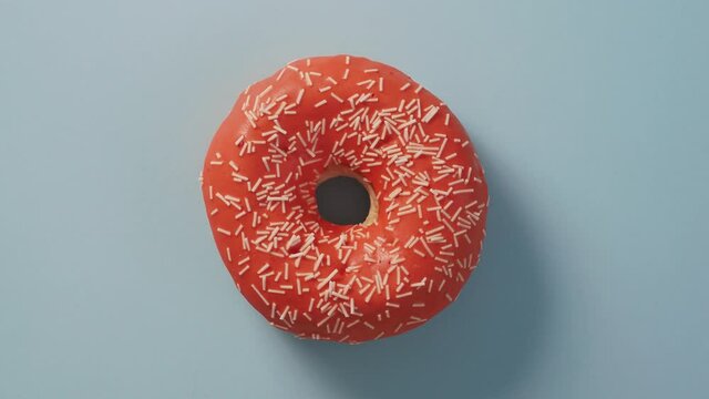 Orange glazed donut rotating on blue, top view