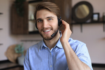 Cheerful young support phone male operator in headset, at workplace while using laptop