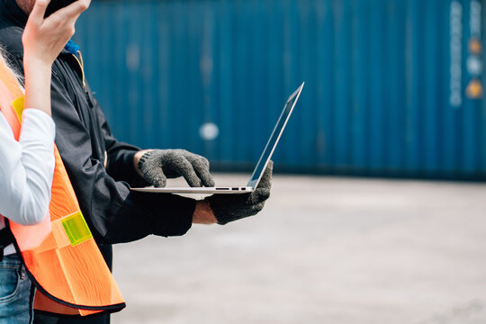 Closeup hand worker in safety jumpsuit using laptop check container at cargo shipping warehouse. transportation import,export logistic industrial service