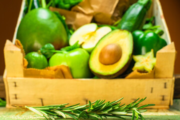 Rosemary in foreground with green fruits and vegetables crate in back ground