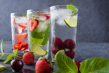 Three glass of refreshing cool detox drink with strawberry, lime, cherry and mint on dark background. Various summer lemonades or ice tea. Mojito cocktails with ice cubes. Healthy eating. Top view