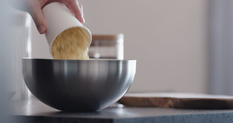 man making granola pour wheat flakes into steel bowl on kitchen countertop