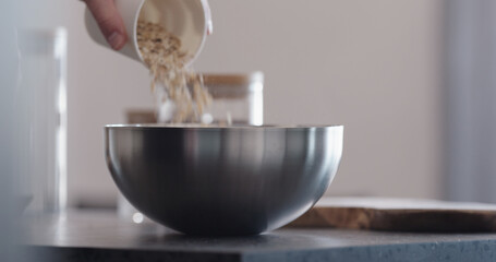 Man making granola pour oat flakes into steel bowl on kitchen countertop