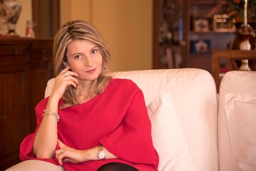Ritratto di una donna bionda con un vestito rosso seduta sul divano.