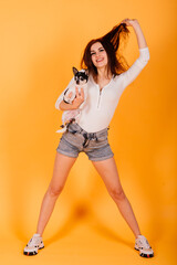 Beautiful young woman holding her dog on yellow background.