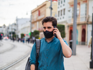 Spanish male with face mask talking on the phone outdoors - concept of the new normal