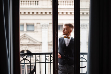Confident groom in wedding suit standing on hotel balcony