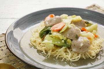 A plate of I Fu Mie or Crispy Fried Noodle with thick savory sauce and meatball and vegetables in shiny and grainy white background. Selective focus