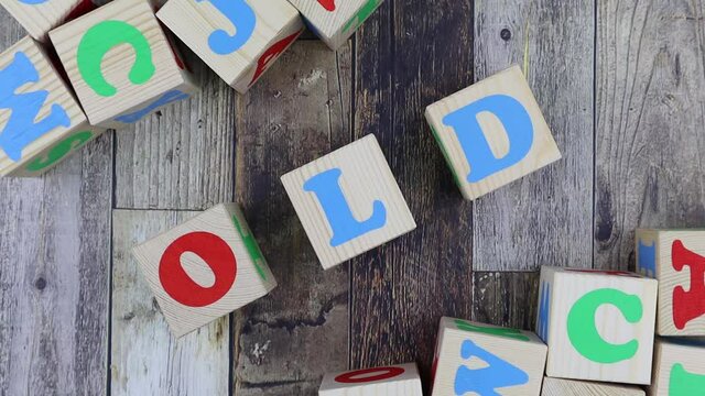 Colourful alphabet letters on wooden cubes with word - Old - in a diagonal line with additional blocks decorating the corners of the frame. Stop motion, top view