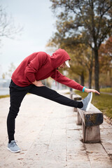 Athletic sporty man training in hoodie sweatshirt in urban city park.