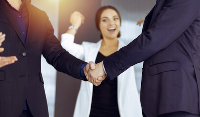 Unknown businesspeople are shaking their hands after signing a contract, while standing together in a sunny modern office, close-up. Business communication concept