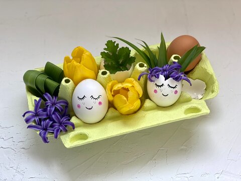 children's DIY, spring decor with eggs with eyes and flowers, in a box recycled from eggs.