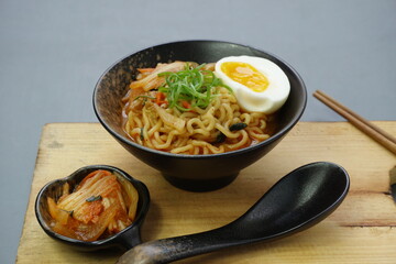 Ramyeon or Korean instant noodle with Kimchi on black bowl. Isolated in gray background, wooden board and chopstick