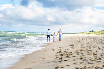 A little girl and her parents walk on the beach on the Baltic Sea in Lithuania