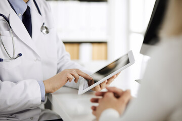 Unknown male doctor and patient woman discussing current health examination while sitting in clinic...